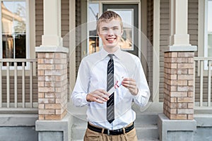 Young male student holding a diploma in front of a house while wearing a dress shirt and a tie.