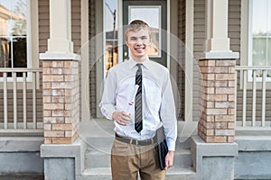 Young male student holding a diploma and a graduation cap in front of a house.