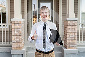 Young male student holding a diploma and a graduation cap in front of a house.
