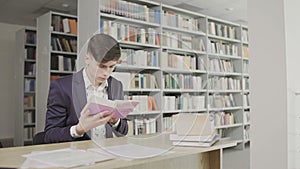 Young male student reading a book in a library. Man in a suit reading book on bookshelf background.