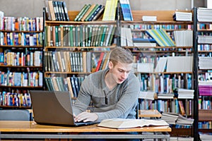 Young male student typing on laptop in the university library