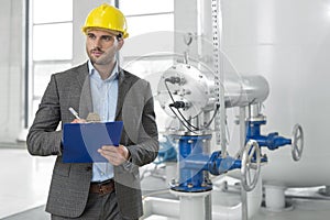 Young male supervisor writing on clipboard in industry