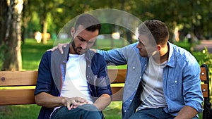 Young male supporting friend sitting outdoors together, friendship care, advice