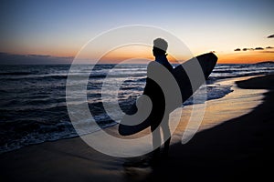 Young male surfer on beach in sunset