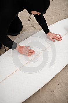 Young male surfer wearing a wetsuit bent over his white surfboard