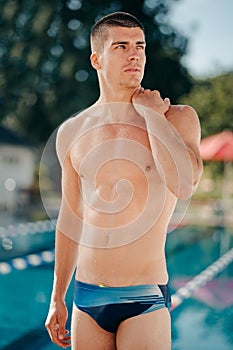 Young male swimmer wearing a swimsuit and standing near a swimming pool