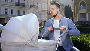 Young male swinging baby stroller trying to calm down crying infant, parenting