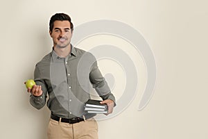 Young male teacher with books and apple on beige background