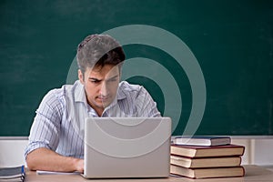 Young male teacher in front of green board