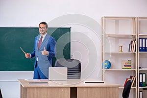 Young male teacher in suit in front of green board