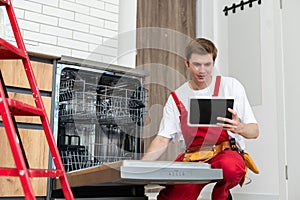 Young Male Technician Checking Dishwasher With Digital Multimeter In Kitchen