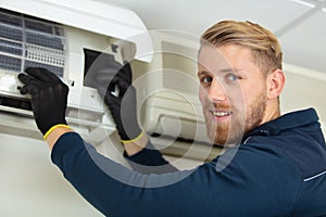 young male technician repairing air conditioner wearing black gloves