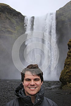 Young male tourist aged 20-25 poses in front of skogafoss waterfall in Iceland. Iceland has become a popular tourist