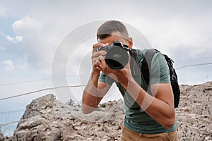 A young male tourist with a backpack climbed to the top of the mountain and takes pictures on the peak from a height