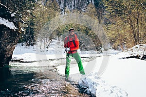 Young male tourist crosses a river in the mountains in winter