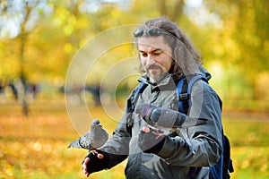 Young male tourist feeding pigeons in St James`s Park in London, United Kingdom, on beautiful sunny autumn day