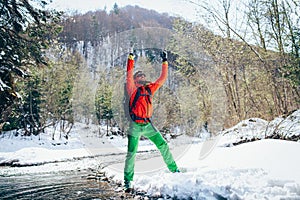 Young male tourist raises his hands near a river in the mountains.