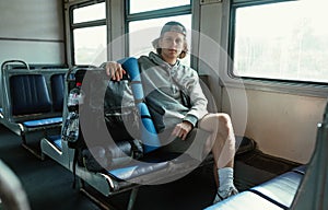 Young male tourist sits in a train in a train with a tourist backpack and goes on a trip