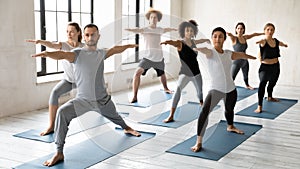 Young male trainer leading yoga class for concentrated multiracial students.