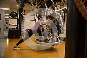 Young male trainer teaching mature woman doing sport exercise on hanging mat