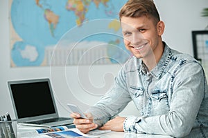 Young male travel agent consultant in tour agency holding smartphone