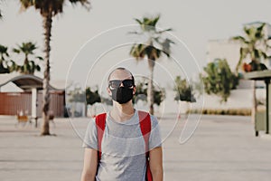 Young male traveler with backpack and in sun glasses wearing black protective mask