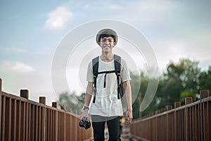 Young male traveler photographer smiling walking on wooden bridge with backpack and holding a camera