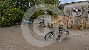 Young male traveler rides a bike down a flooded street in Maldives.