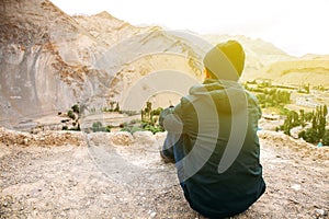 Young male traveler sitting on the sand cliff, thinking about something in Leh, Ladakh, India