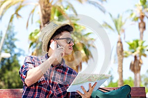 Young male traveler talking on mobile phone and holding map