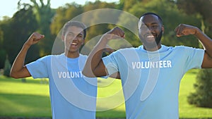 Young male volunteers showing arm muscles, strength gesture, teamwork support