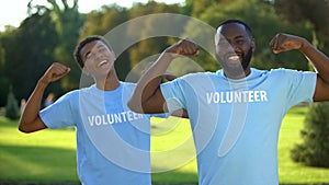 Young male volunteers showing arm muscles, strength gesture, teamwork support