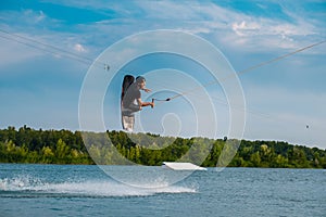 Male wakeboarder jumping over water with board holding rope
