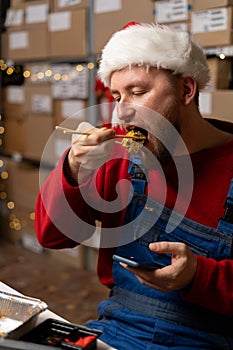 Young male warehouse worker having lunch at workplace eating delicious fresh sushi rolls, food delivery concept