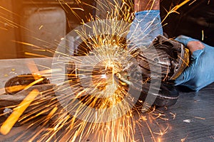 A young male welder in a white working gloves grinds a metal product with angle grinder in the garage