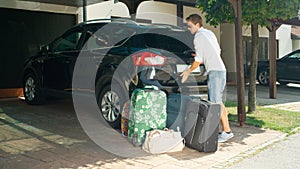 Young male in white shirt closes the trunk of his car parked in front of house.