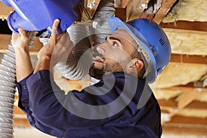 young male worker installing air conditioning unit into roof space