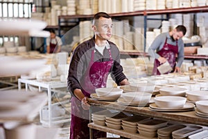 Young man moves rack with ceramic blanks photo