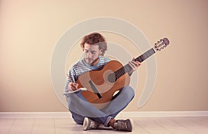 Young man with acoustic guitar composing song near wall