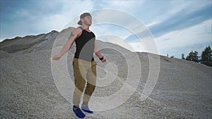 Young man actively jumping rope in nature on a summer day with stone background