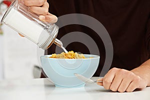 Young Man Adding Sugar To Breakfast Cereal