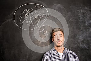Young man against the background of chalkboard solving a problem