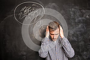 Young man against the background of chalkboard solving a problem