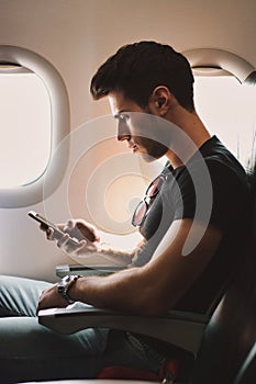 Young man against plane window using cell phone