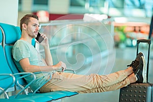 Young man in an airport lounge waiting for flight aircraft. Caucasian man with smartphone indoor
