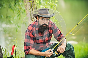 Young man angler fishing. Fisherman with rod, spinning reel on river bank. Man catching fish, pulling rod while fishing