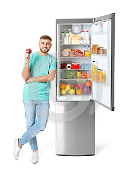 Young man with apple near open refrigerator
