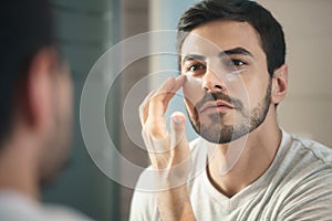 Young man applying anti-aging lotion fot skin care