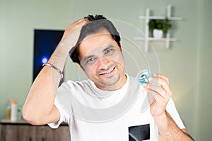 Young man applying gel to hair to protect from hair loss or dandruff by looking at camera - concept of hairstyle setting