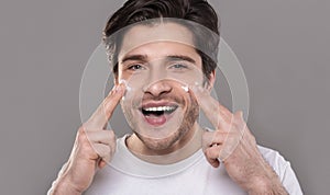 Young man applying moisturizer cream on his face